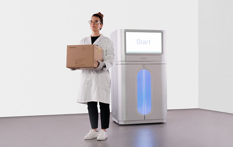 Lab scientist standing by NovaSeq X Plus Sequencing System holding the most sustainable packaging from Illumina yet